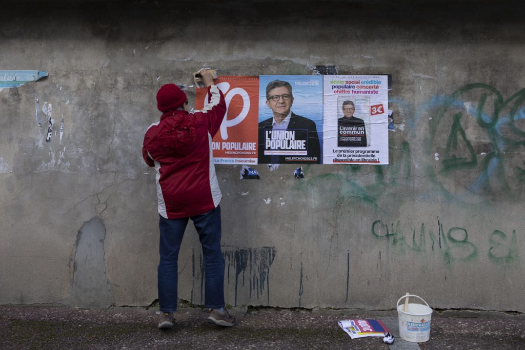 Un membre du comité de soutien de Jean-Luc Mélenchon colle des affiches sur un mur d'affichage public.