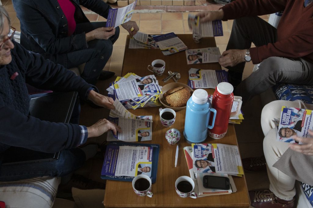 Des membres du comité de soutien de Jean-Luc Mélenchon préparent des tracts posés sur une table basse.