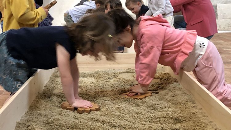 Des enfants appuient sur des formes en bois pour imprimer leurs traces dans un bac à sable en bois.