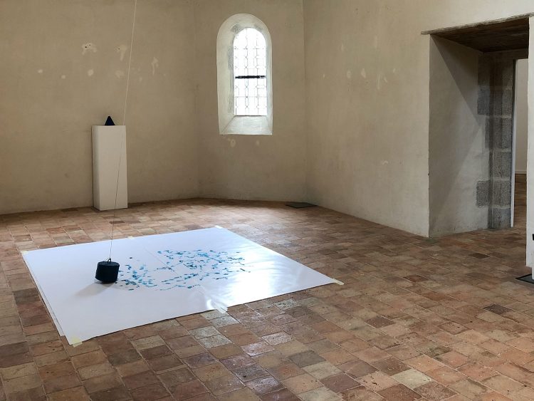 Dans un coin de la chapelle, une grosse craie grasse bleue est reliée à un fil accroché au plafond. Au sol, des traces bleues ont fait leur apparition sur un grand carré de papier.