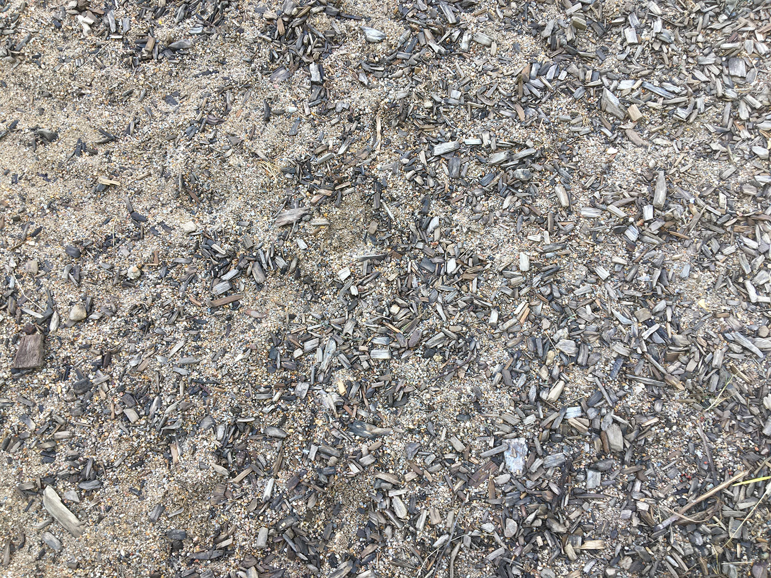 Gros-plan sur le sable et les copeaux qui recouvrent le sol d'une partie de la cour de récréation.