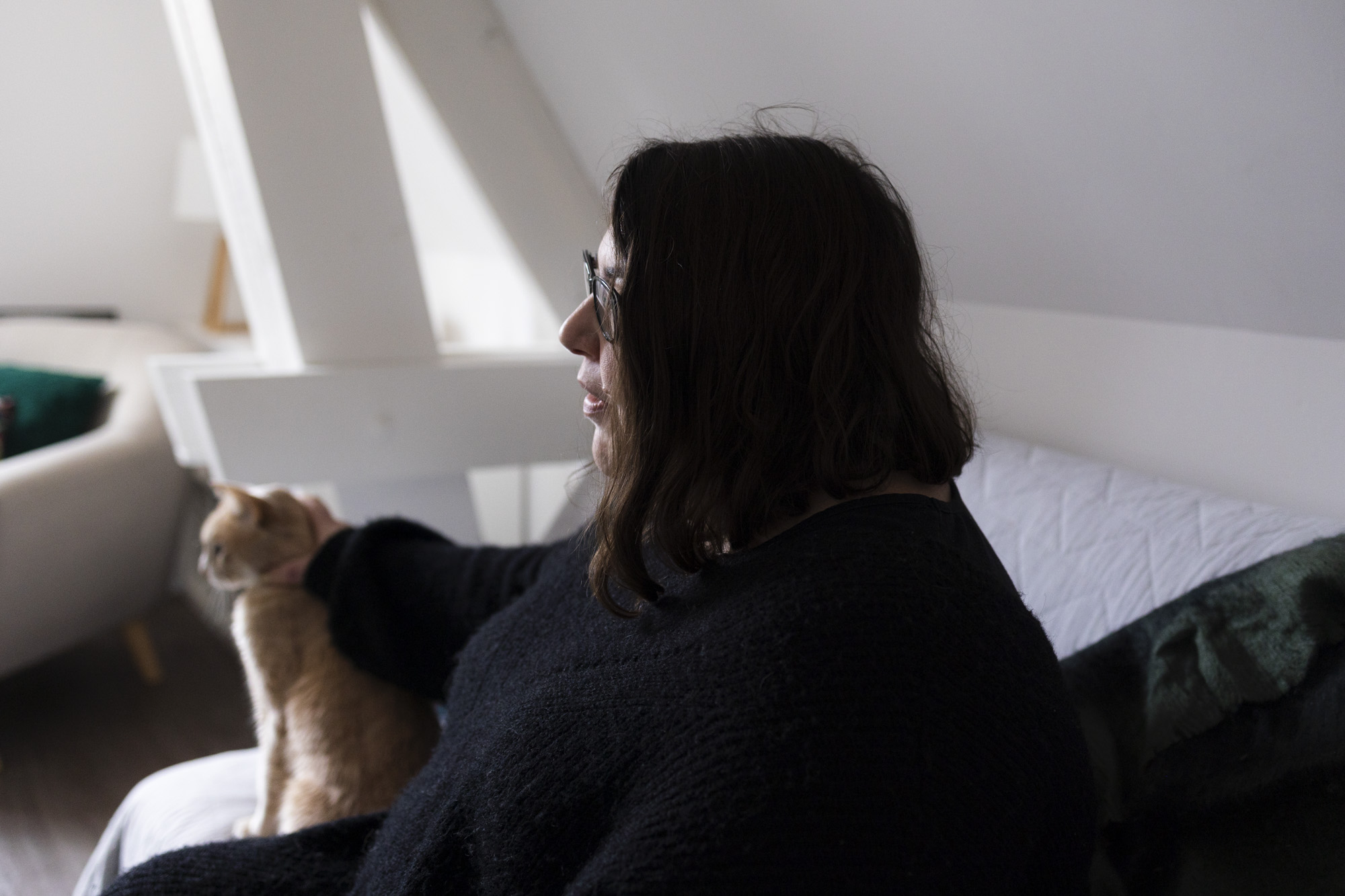 Emilie dans son logement social à Chartres. Vêtue d'une longue robe noire, elle est assise sur son canapé en caressant son chat. 