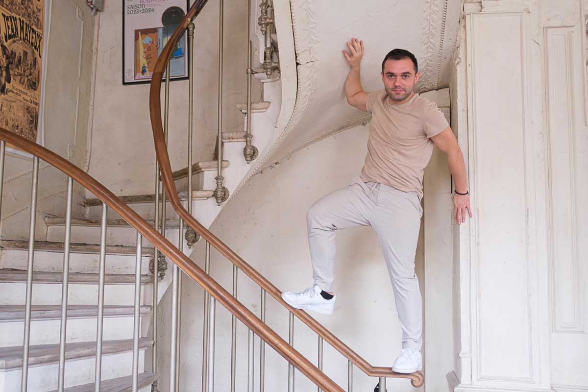 Alexandre Liberati, comédien, pose debout sur la main courante d'un escalier en pin et bois blanc.