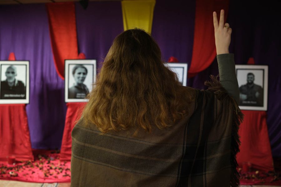 Piya O. (de dos) pose devant les portraits des 6 militants kurdes assassinés en 2013 et 2022.